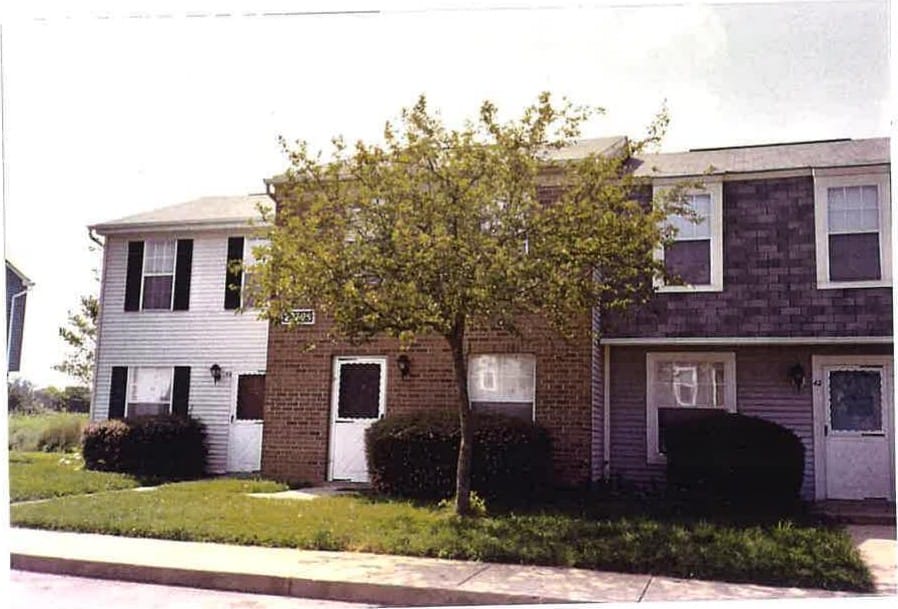 A row of two-story Leonardtown Village townhouses with brick and light siding, framed by a shade tree