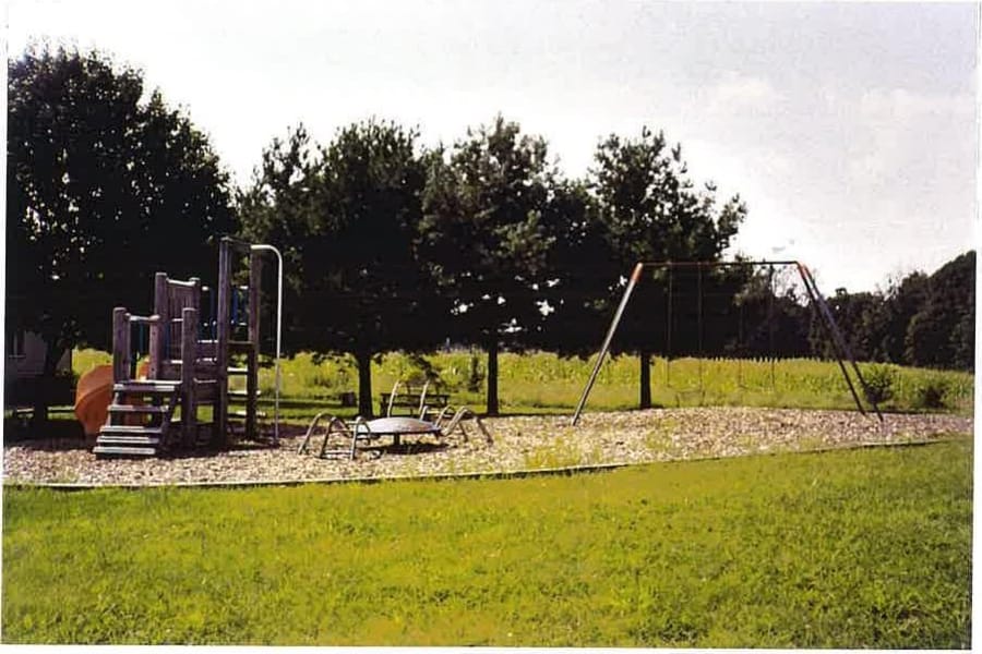 The community playground at Leonardtown Village, with a climbing frame and swings on an open, tree-lined lawn